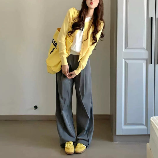 Woman wearing a yellow jacket and gray pants in a room with a white wall and door.