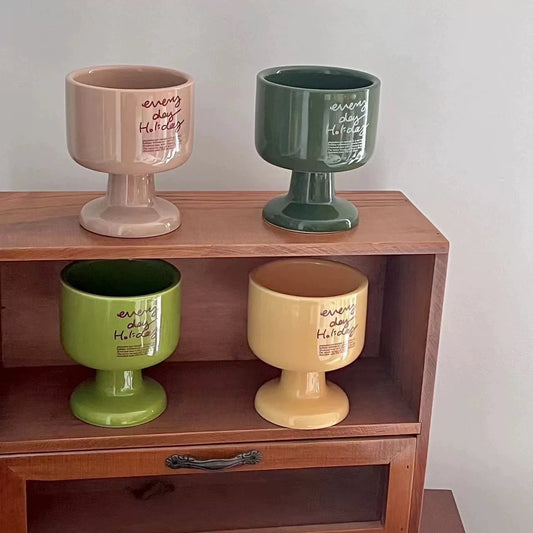 Four ceramic cups in different colors on a wooden shelf with a plain background